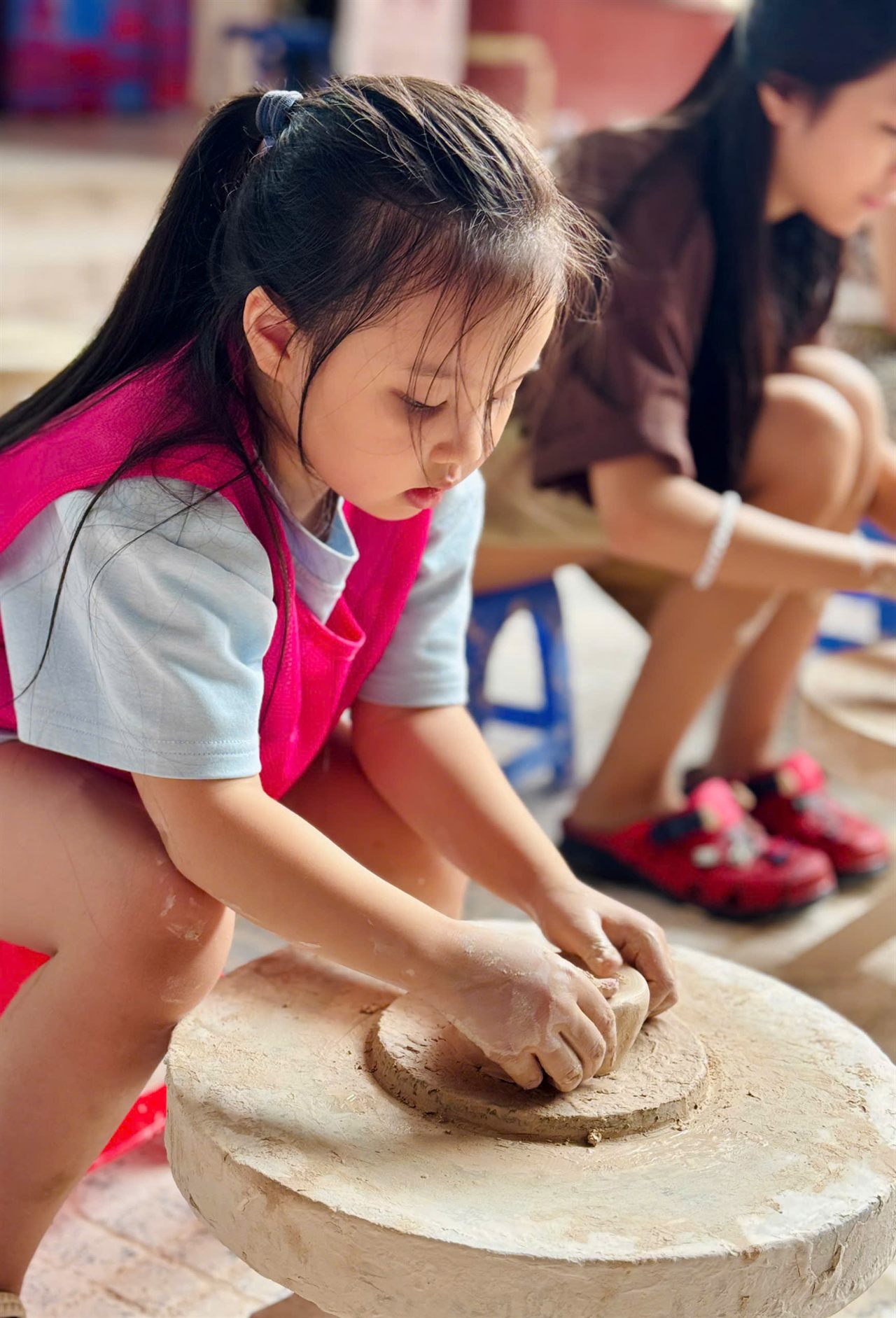 Bé gái chăm chú nặn đất trên bàn xoay gốm